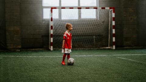 A boy standing next to a soccer ball near a soccer net.